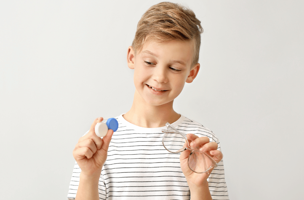 young kid holding glasses in one hand and a contact lens case in the other