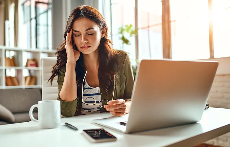 a tired woman at work holds her hand to her head due to a headache