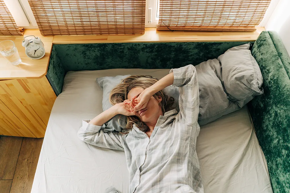 a woman lying in bed in the morning rubbing her eyes