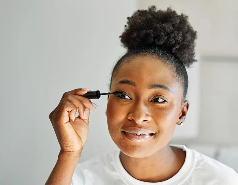 a woman putting on mascara at home