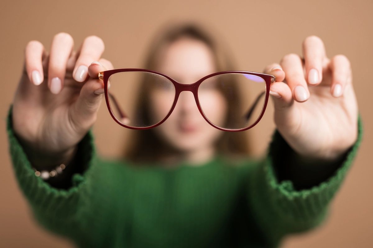 nearsightedness Poor vision concept, Young girl with poor vision holds glasses with hands forward on beige background